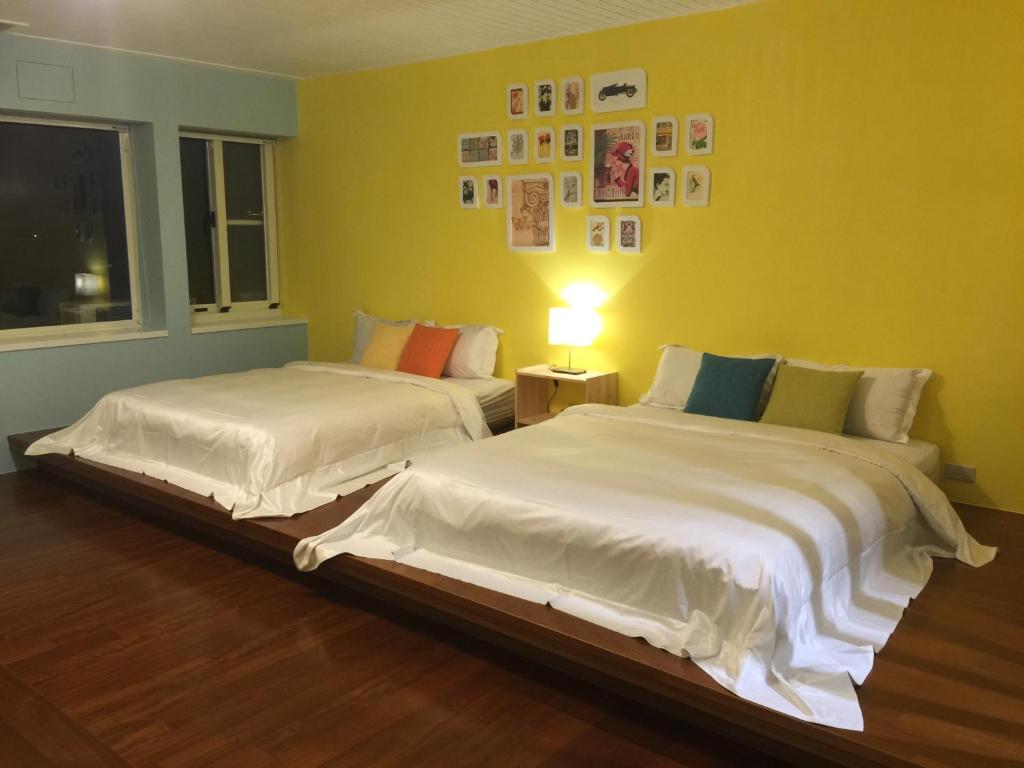 two beds in a room with a yellow wall at Pottery B&amp;B in Jiaoxi