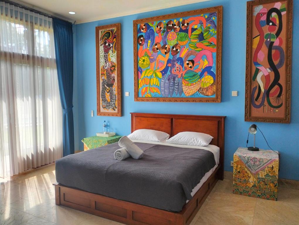 a bedroom with a large bed with paintings on the wall at Villa Biyu siyu in Ubud