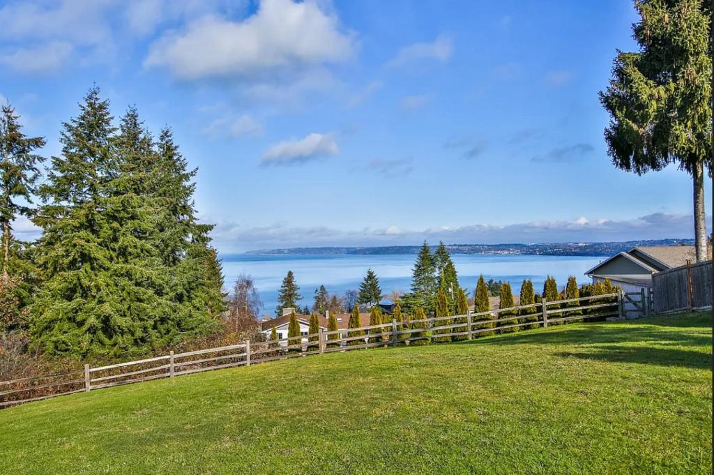 a field with a fence and a view of the water at Oceanline 180° home in Federal Way