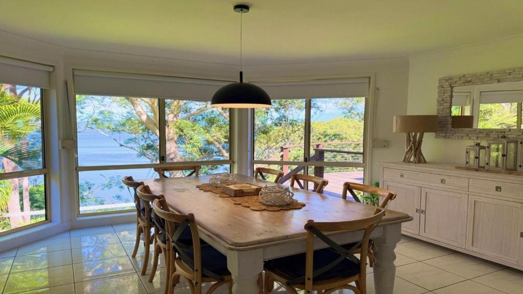 Un comedor con mesa y sillas y ventanas. en Luminara Luxury Lakefront, en Smiths Lake