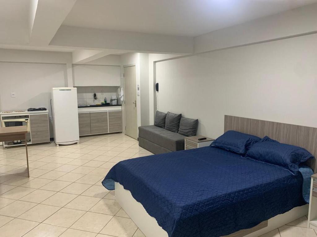 a bedroom with a blue bed and a kitchen at Studio amplo e aconchegante no bairro aterrado in Volta Redonda