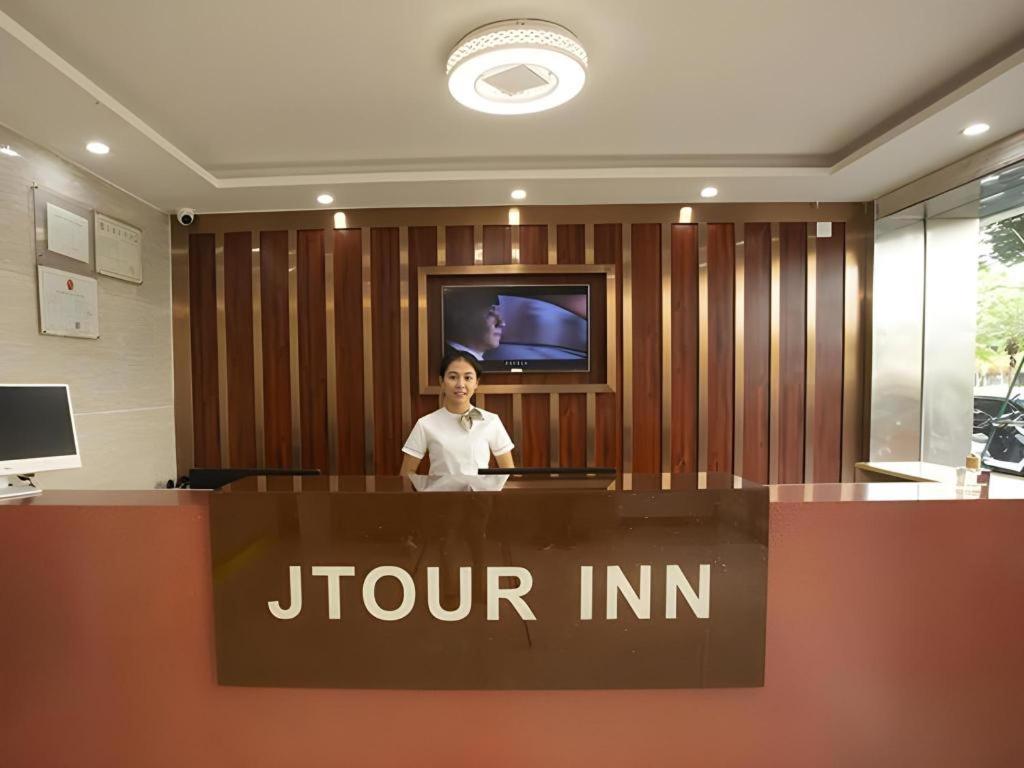a woman is standing behind a jointini sign in an office at JTOUR Inn Zhanjiang Poly Yuandian Plaza in Zhanjiang