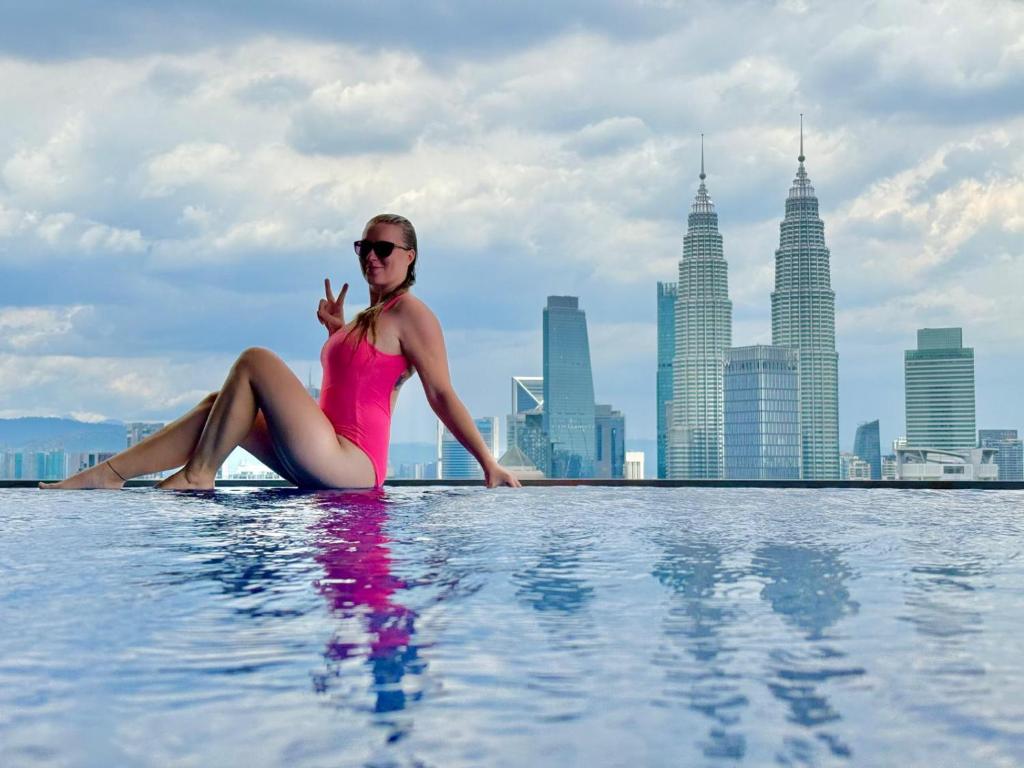a woman sitting in a infinity pool with a city skyline at The Luxe Colony KLCC by Rsafa in Kuala Lumpur