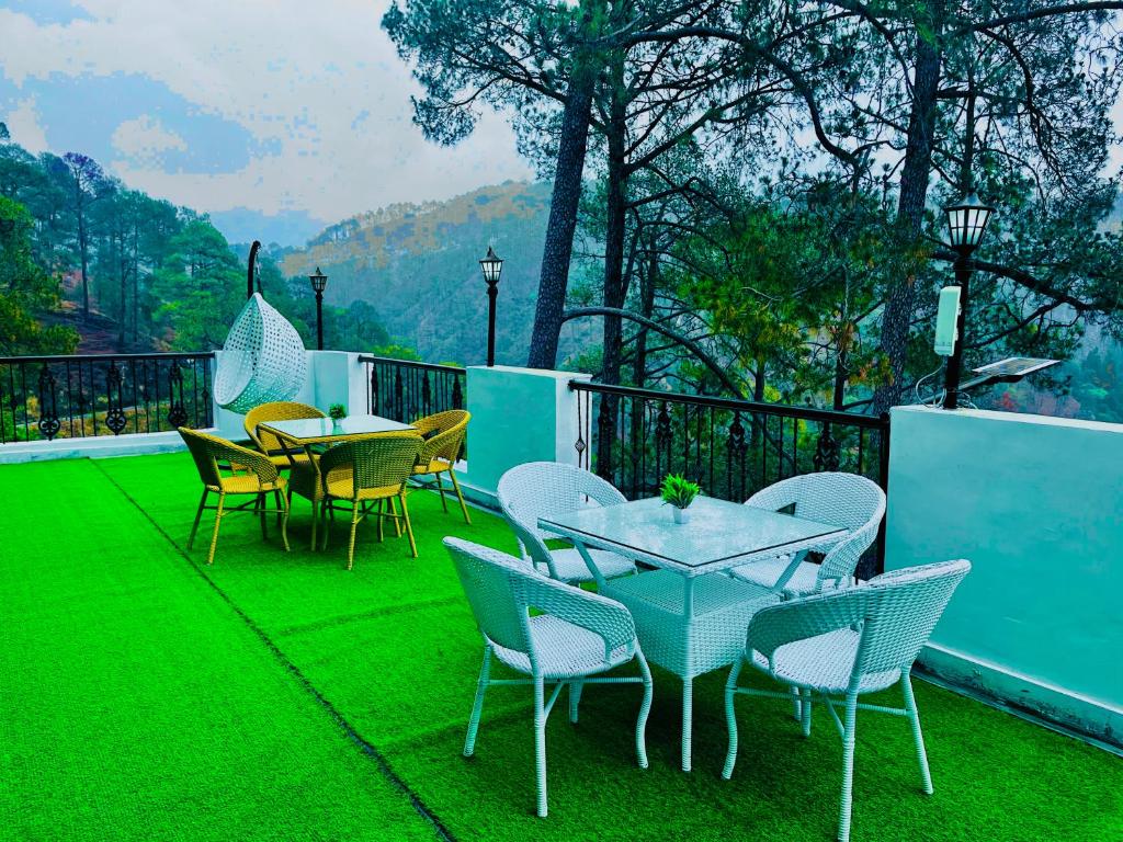 Un grupo de mesas y sillas en un balcón con césped verde. en The Ambience Resort, Nainital - A Hidden Gem Away From City Hustle, en Nainital