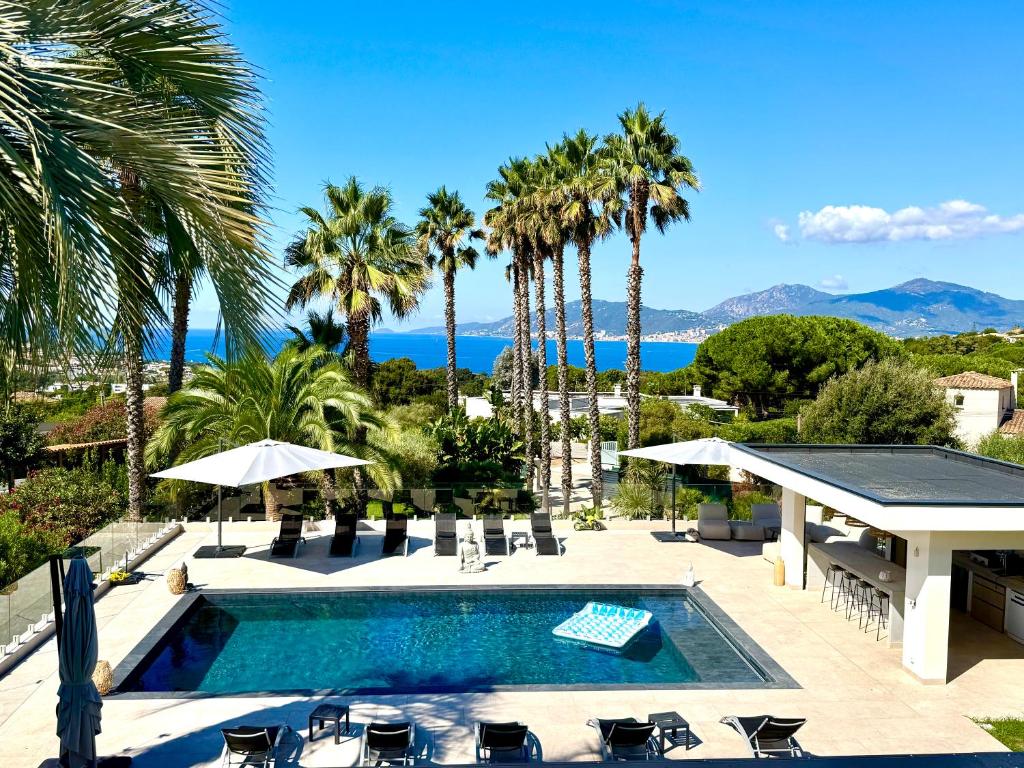 a pool with chairs and palm trees and the ocean at villa NOESIS in Grosseto-Prugna