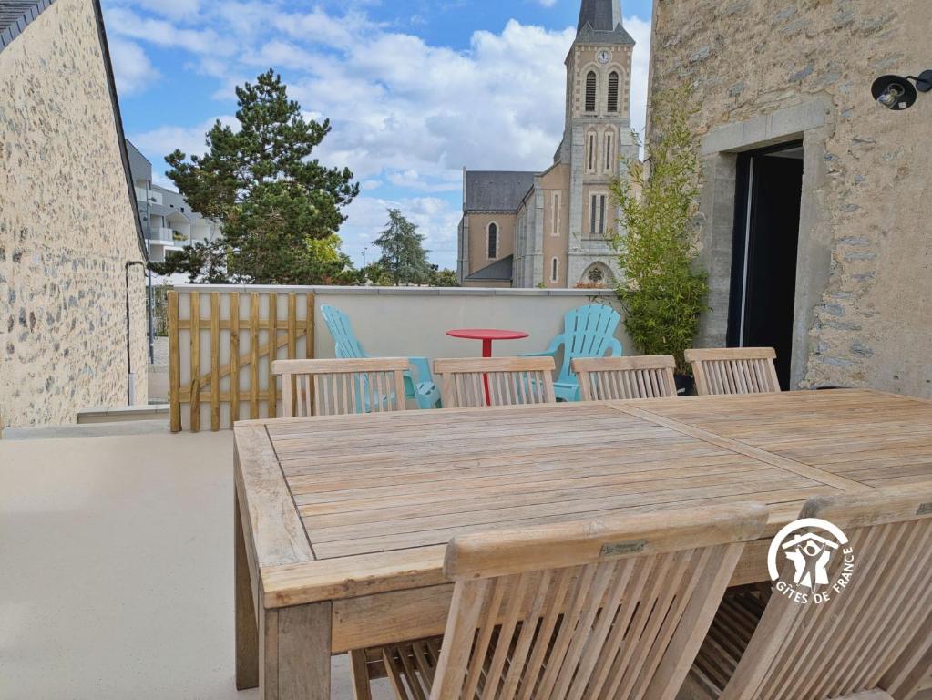 une table et des chaises en bois sur une terrasse avec une église dans l'établissement Gîte Le 47, 6 à 8 personnes, à Louverné