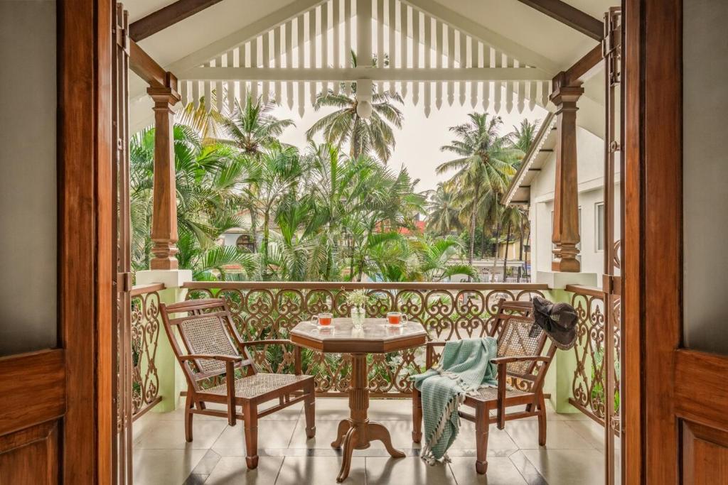 a balcony with a table and chairs and palm trees at Sanctuary by RÊVE in Siolim
