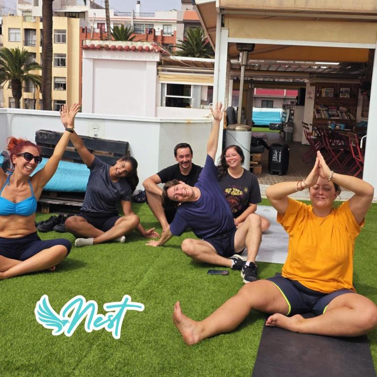 a group of people sitting on the grass with their hands in the air at Aguere Nest Hostel in Las Lagunas