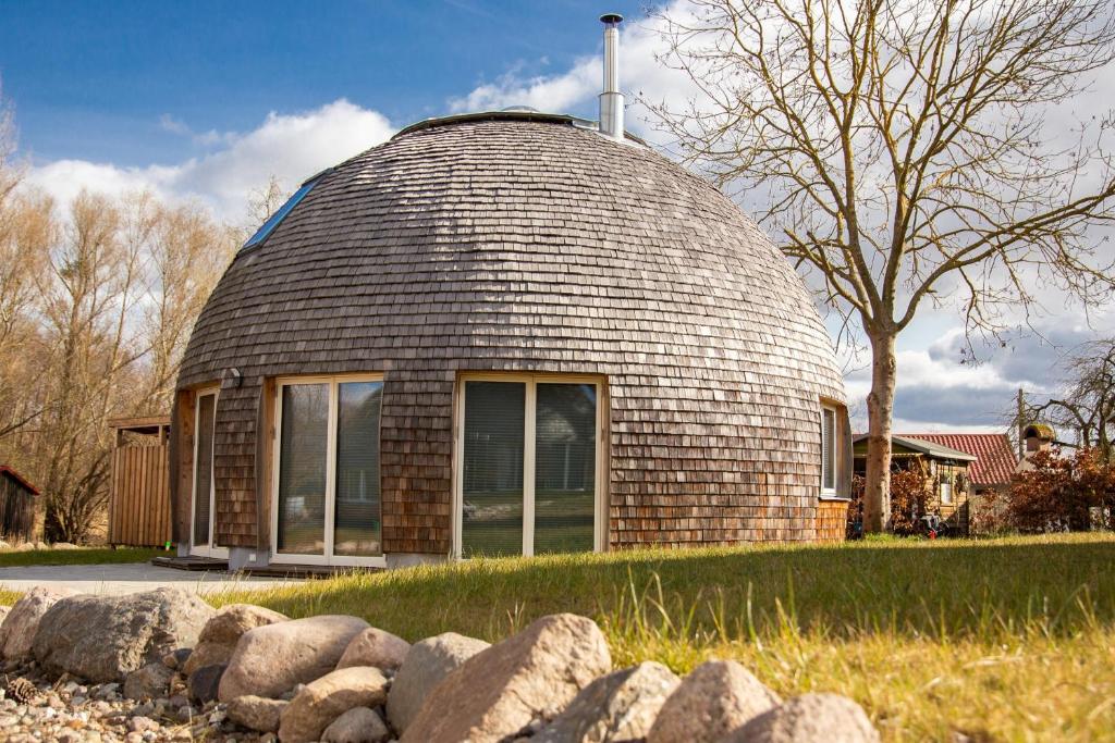 Una casa abovedada con una valla de piedra delante. en Kugelhaus Phoebe Charmantes Kugelhaus aus Holz am Waldrand des Tollensesees, en Wustrow