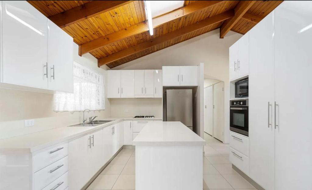 a white kitchen with white cabinets and a wooden ceiling at Ella sweet home in Algester
