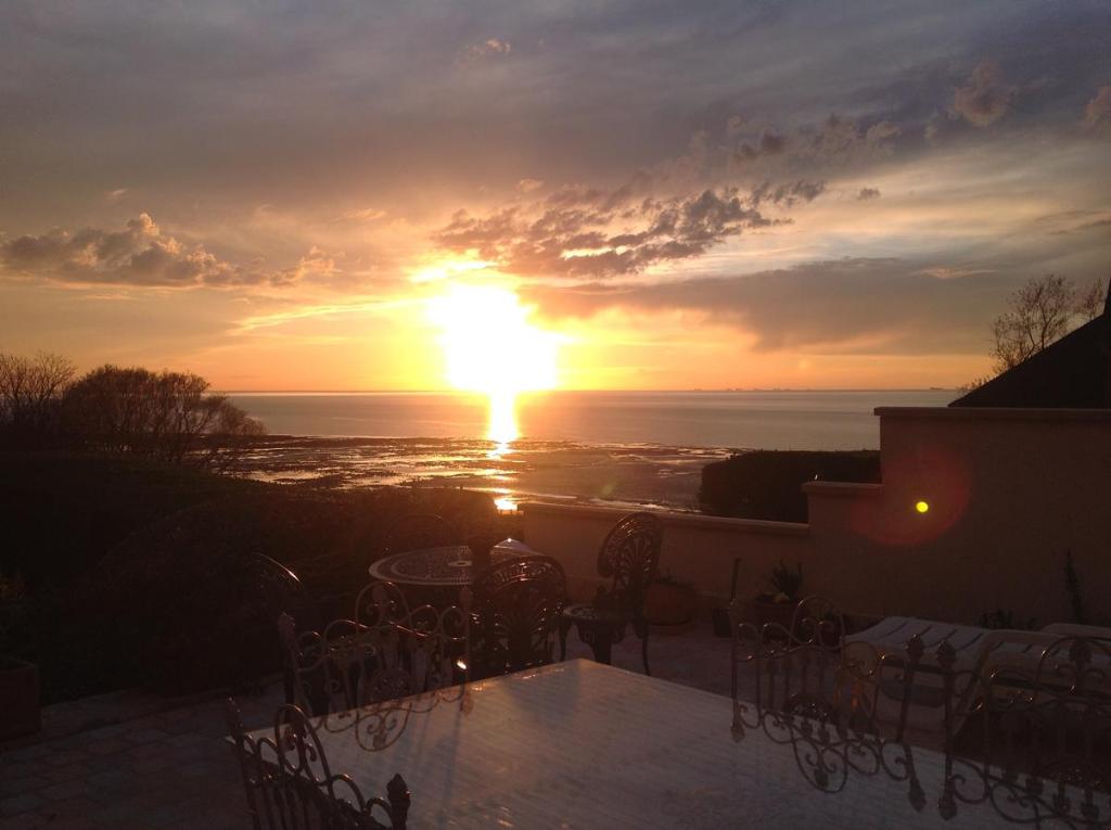 a sunset from a patio with a table and chairs at Appartement terrasse face mer in Villerville