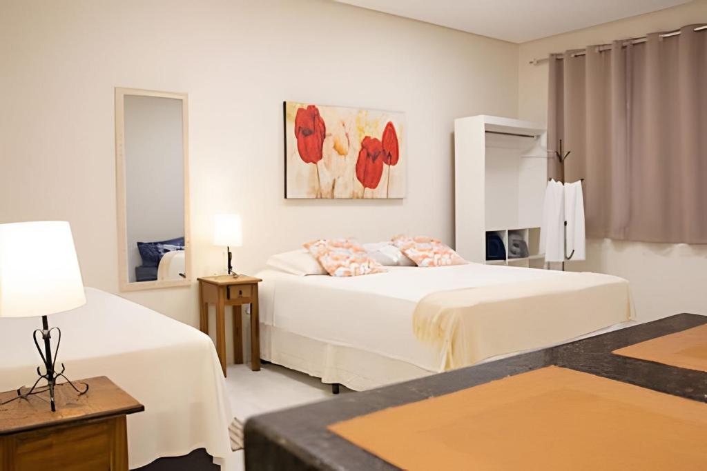 a white bedroom with two beds and a table at Flats Premium Jabaquara in Paraty
