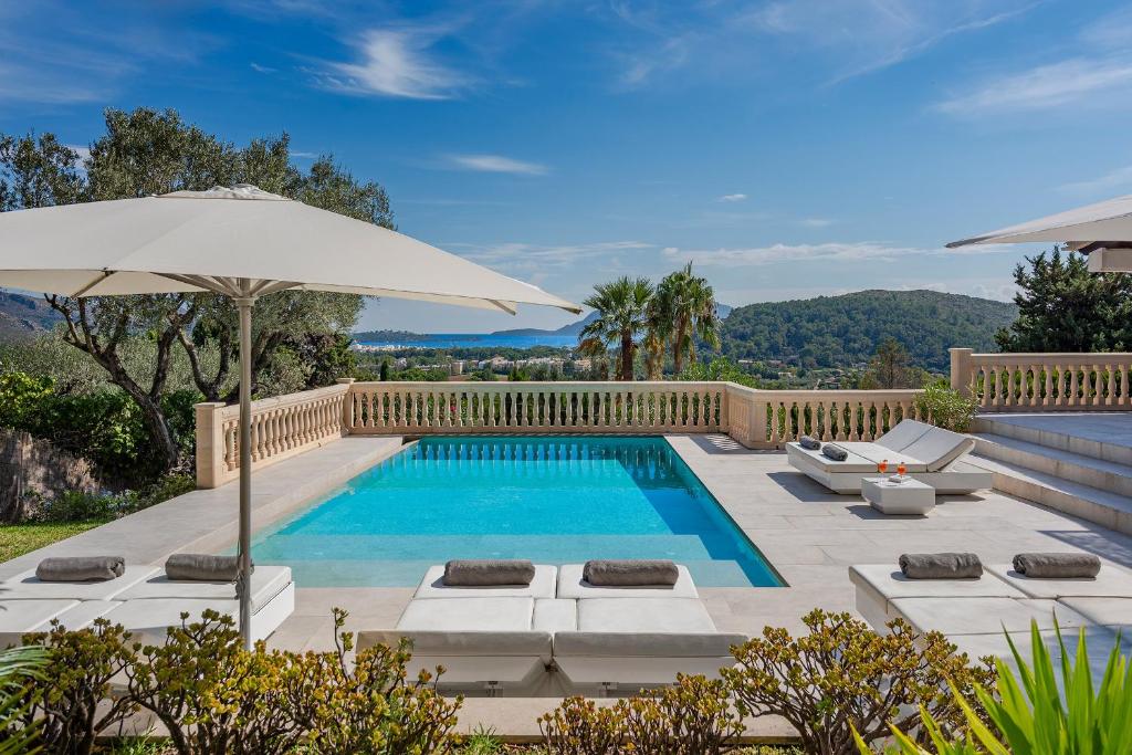 a swimming pool with an umbrella and lounge chairs next to it at Villa Bonjour in El Port