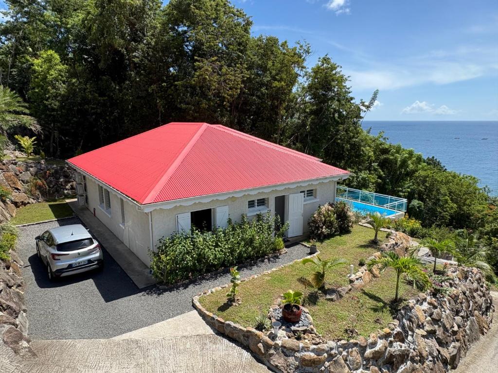 a small house with a red roof next to the ocean at Villa Ti'Kawet in Pointe-Noire