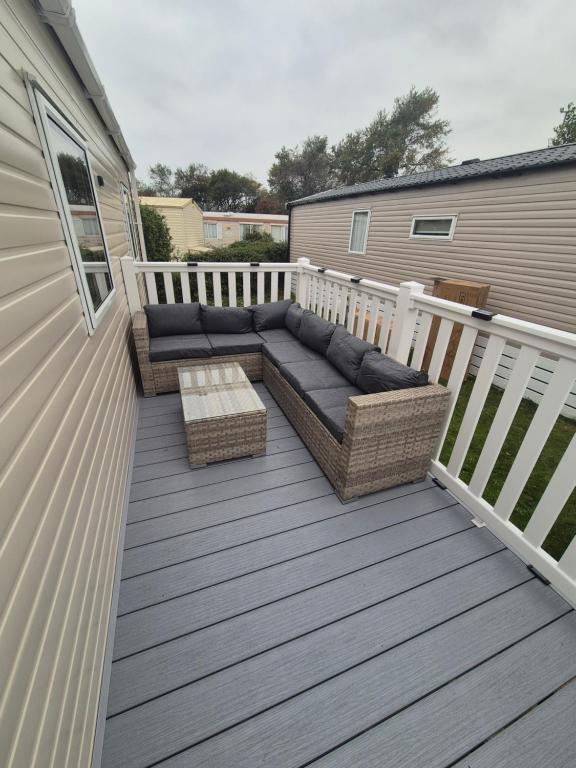 a patio with a couch and a table on a deck at Meadow Banks Combe Haven in Hastings