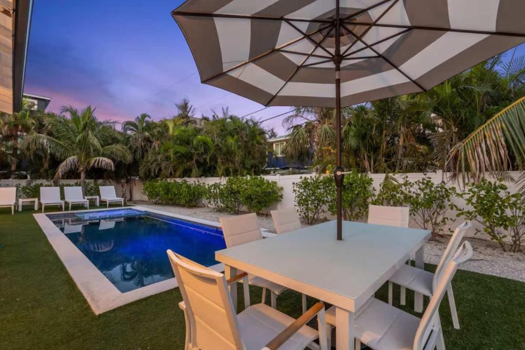 a table with an umbrella next to a swimming pool at Honey I'm Holmes - New Home Near the Beach Turf in Anna Maria Island