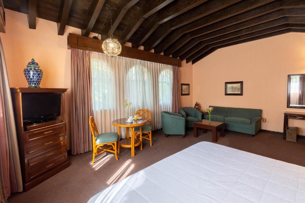 A traditional bedroom combines a large bed with a sitting area beneath exposed dark ceiling beams.