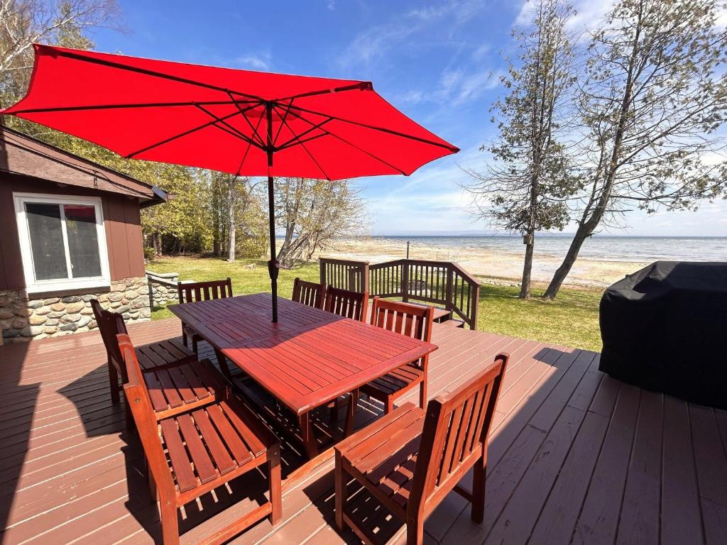 a wooden table with a red umbrella on a deck at Lakeside Lodge in Saint Ignace