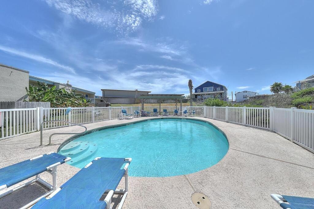 a swimming pool with two blue benches and a fence at Relax Inn-Seamist 156 in Port Aransas