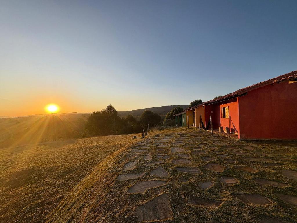 a sunset over a field with a barn and a dirt road at Chalés Pão Sobre as Águas - a 5 minutos de cachoeiras e vista maravilhosa do pôr do sol in Carrancas