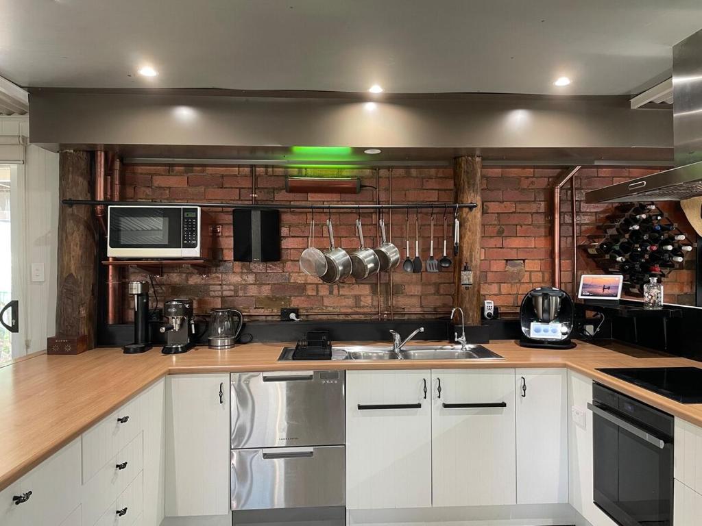 a kitchen with white cabinets and a brick wall at The Orchard Guesthouse in Palmwoods
