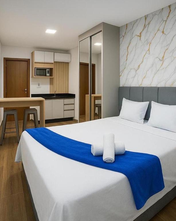 a bedroom with a large white bed and a kitchen at Studio aconchegante com piscina a 350m da praia in Piçarras