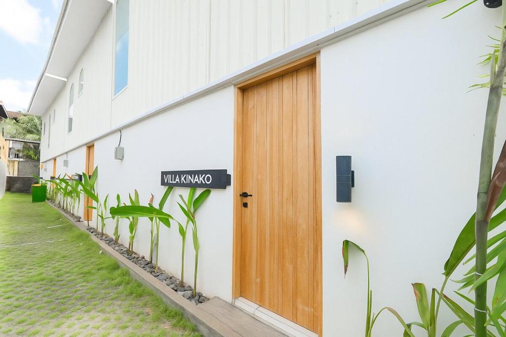 ein weißes Gebäude mit einer Holztür und Pflanzen in der Unterkunft 1BR Stylish Mezzanine Near In Dreamland in Uluwatu