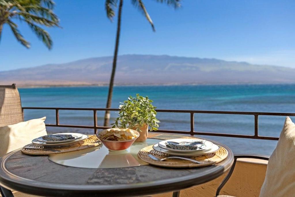 a table with plates and dishes on a balcony with the ocean at Island Sands 210 · IS 210 OceanFront Condo Expansive Ocean Views in Maalaea
