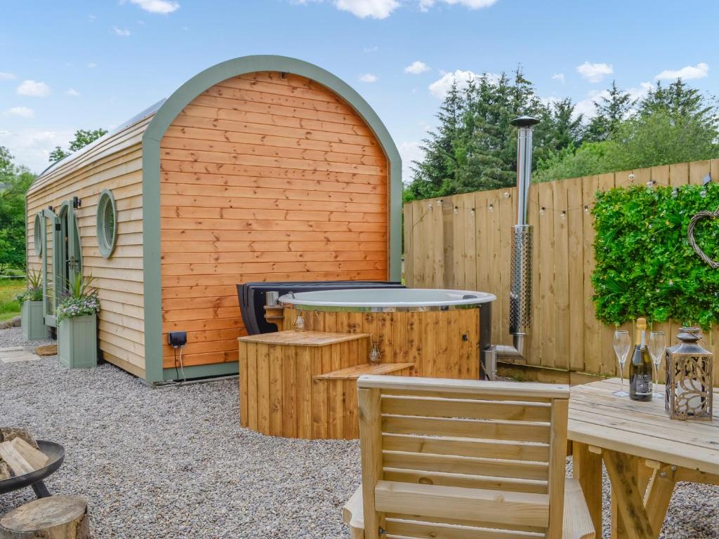 un patio trasero con un cobertizo de madera con mesa y sillas en Bracken - Uk34842, en Straiton