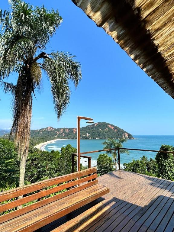 a wooden bench sitting on a deck with a palm tree at Suíte e Sala com Vista para o Mar - Barra do Sahy in São Sebastião
