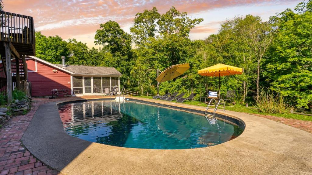ein Swimmingpool mit Sonnenschirm neben einem Haus in der Unterkunft Historic Barn Retreat w Pool Pond Views Longview Pond Lodge by AvantStay in Clinton Corners