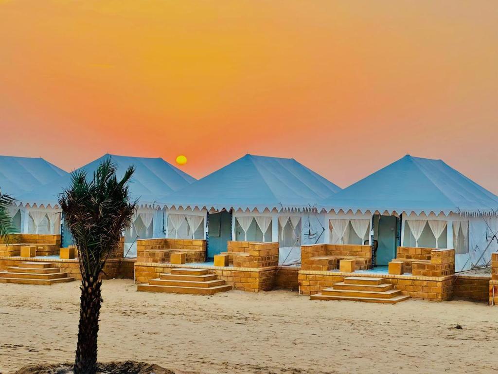 a row of blue tents in the desert with a palm tree at Desert Heritage Sam Camps & Resort in Jaisalmer