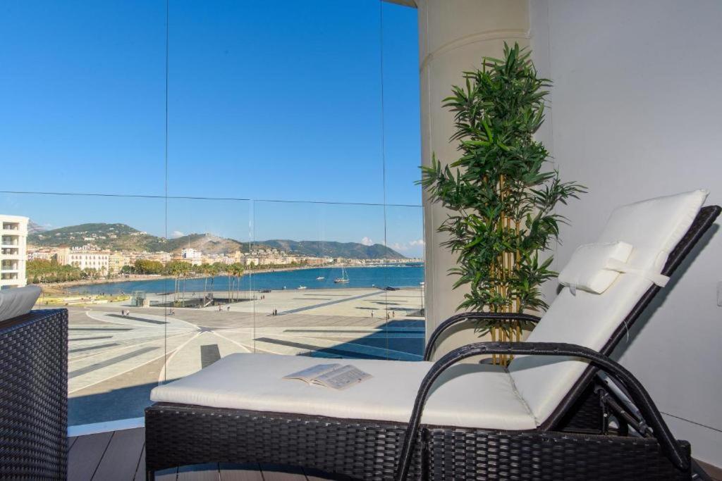 a balcony with a chair and a palm tree at Crescent Luxury Retreat - Seafront Apartments in Salerno