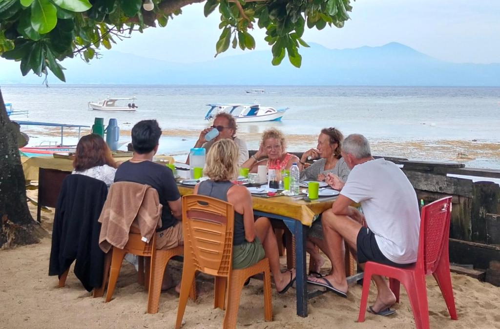 eine Gruppe von Menschen sitzt an einem Tisch am Strand in der Unterkunft Bunaken Coral Homestay in Bunaken