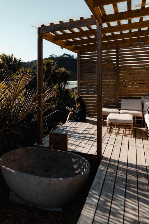 a person sitting on a deck with a tub on a patio at Hahei Tiny Home - Outdoor Bath in Hahei