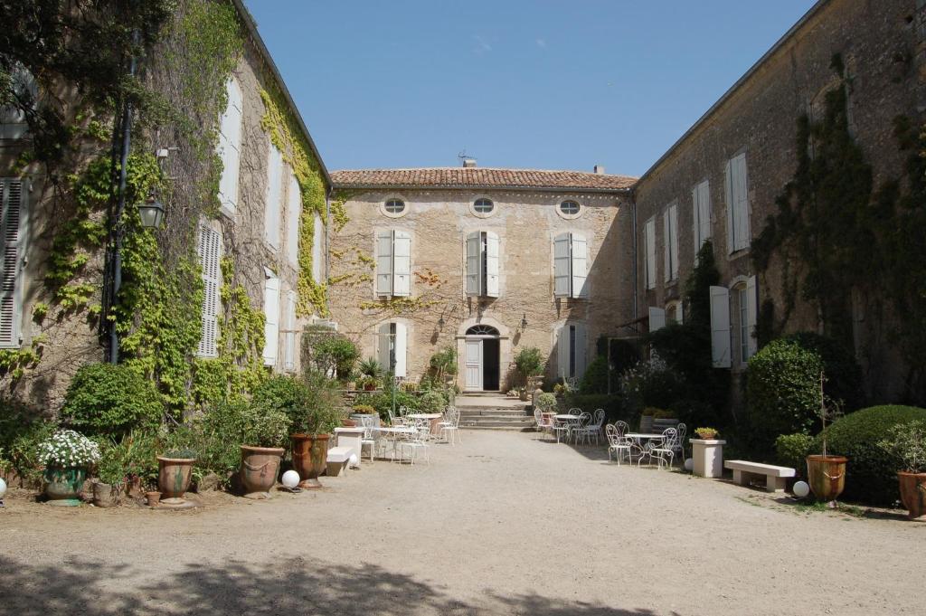 un bâtiment avec une cour agrémentée de plantes, de tables et de chaises dans l'établissement Château Moussoulens, à Moussoulens