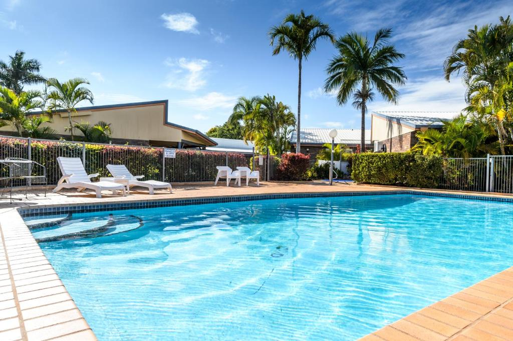 a swimming pool with chairs and palm trees at Smart Motels Bert Hinkler in Bundaberg
