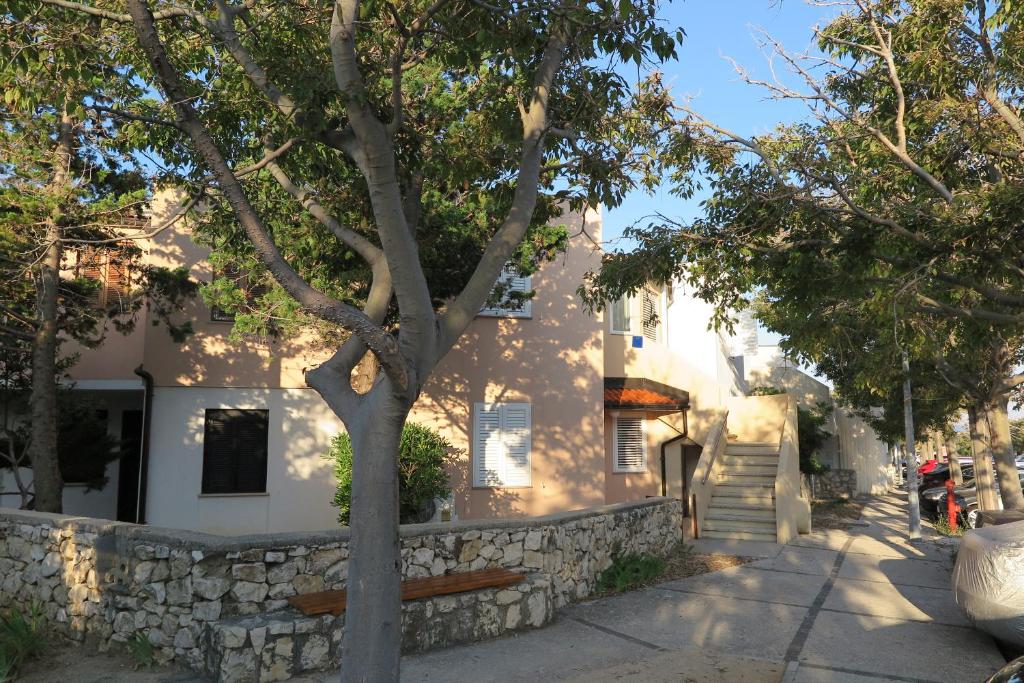 a white house with a stone wall and a tree at Apartment Omerovic in Novalja