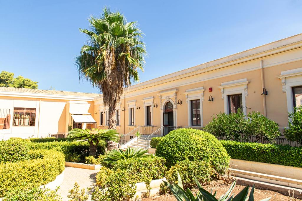 an old building with a palm tree in front of it at Syraka Hotel LR Collection in Siracusa