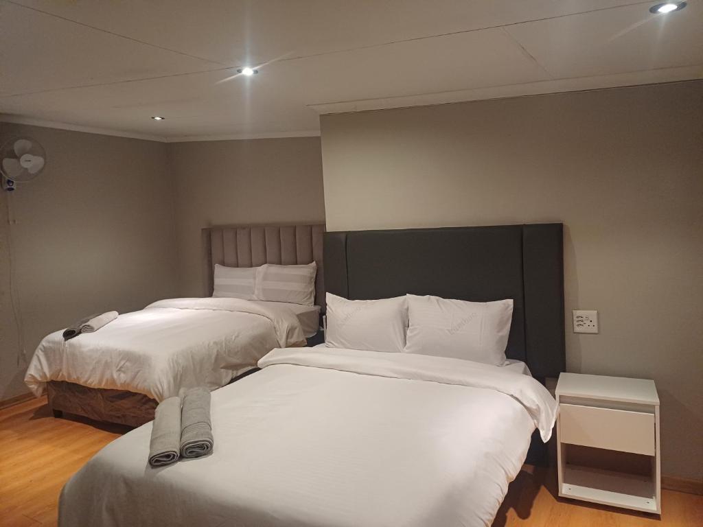 two beds in a room with white sheets and pillows at Blackwood Guesthouse in Vereeniging
