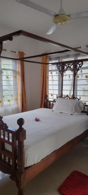 a bedroom with a wooden bed with white sheets and windows at Paul's House in Nungwi