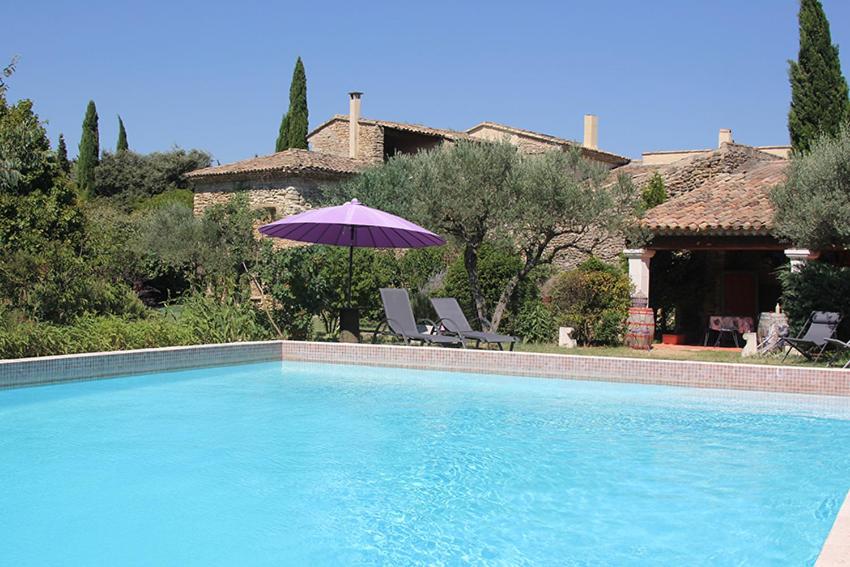 a swimming pool with a purple umbrella and chairs and a house at Maison d'hôtes Ferme de la Commanderie in Richerenches