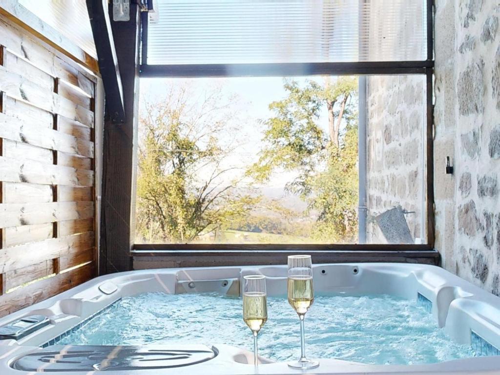 two glasses of wine in a tub with a window at Maison Spa Sauna Proche du Lac in Brive-la-Gaillarde