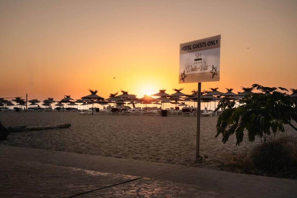a sign on a beach with umbrellas and the sunset at SH Dolce Vita- All Inclusive - Free Aquapark & Beach & Beach bar in Golden Sands