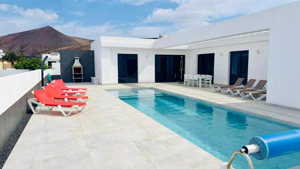 een zwembad met rode stoelen en een villa bij Pipa Costa in Costa Teguise