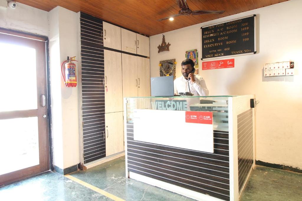 un uomo che parla al telefono dietro un bancone con un computer portatile di Hotel O New Pune a Pune