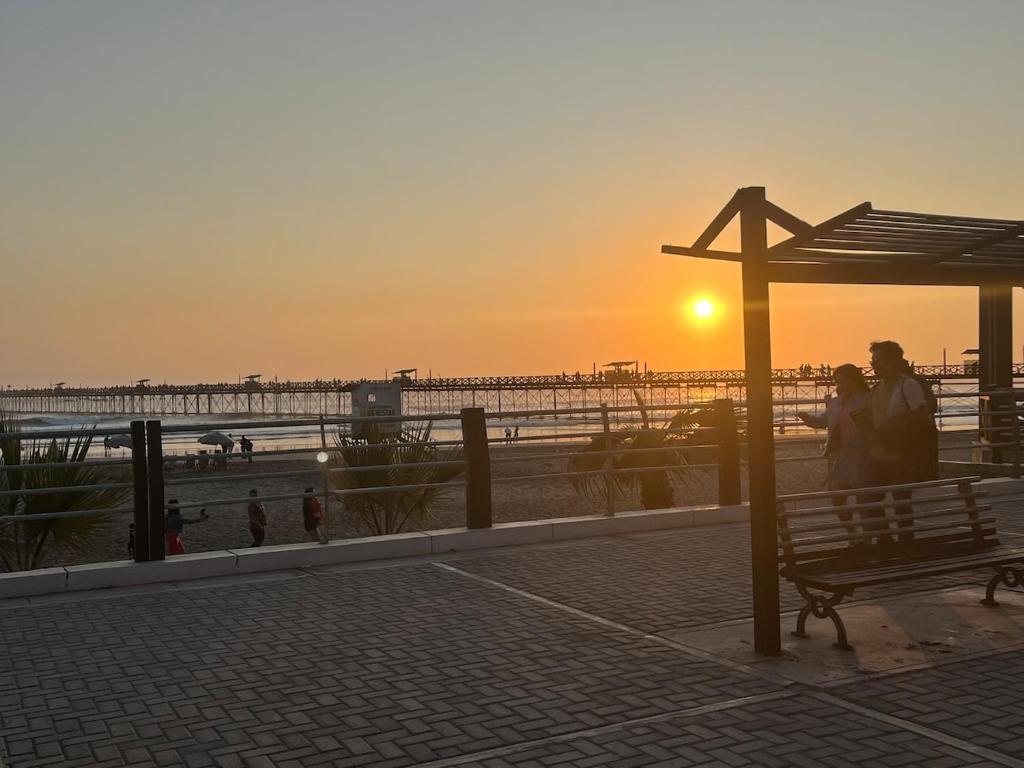 two people standing next to a bench in front of the beach at Pimentel frente al muelle con balcón in Pimentel