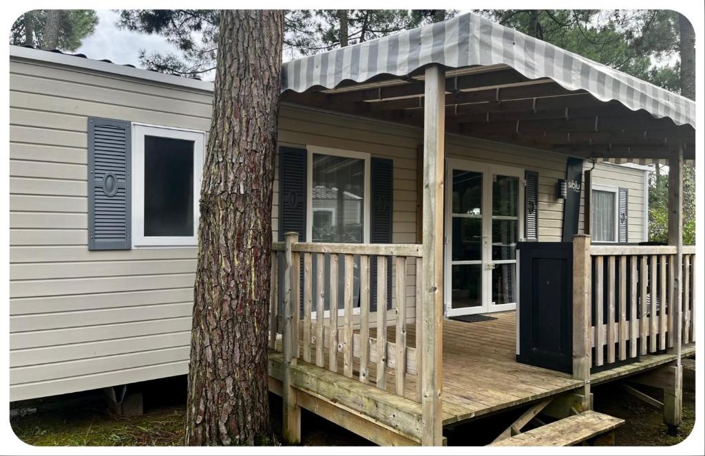 a small house with a porch next to a tree at Mobil home bonne anse plage in Les Mathes