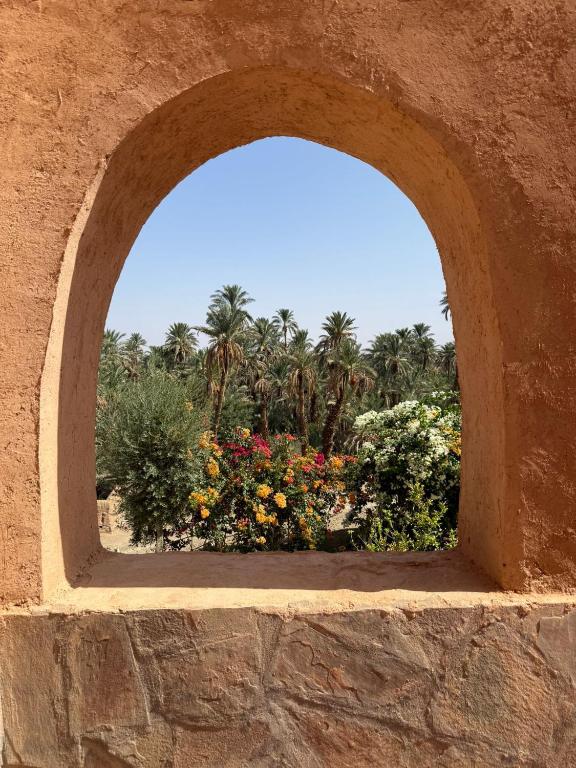 an arch in a stone wall with flowers and palm trees at kasbah panorama chez Alilouch in Nkob