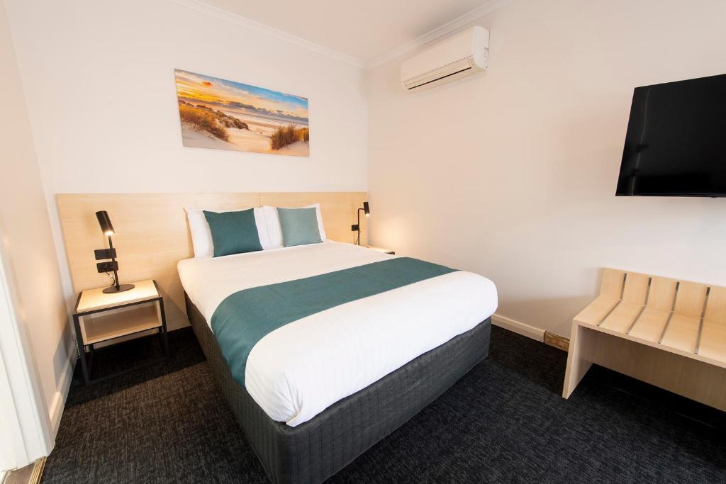 a bedroom with a large bed and a flat screen tv at Glenelg Motel in Adelaide